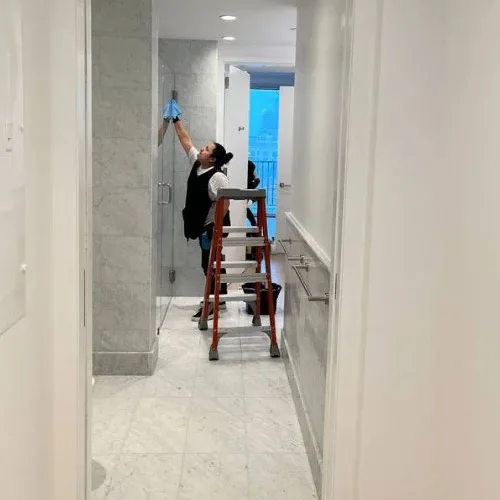 Cleaner on a ladder wiping high surfaces