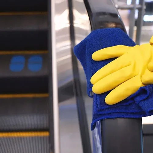 Gloved hand wiping an escalator handrail in a shopping center